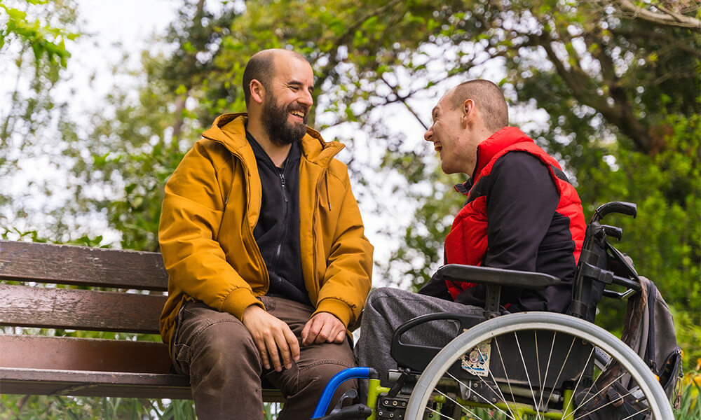 Man sitting on bench laughing with man in wheelchair